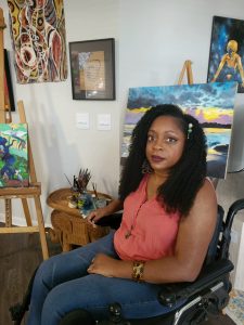 A woman with curly black hair poses in her wheelchair facing the camera.