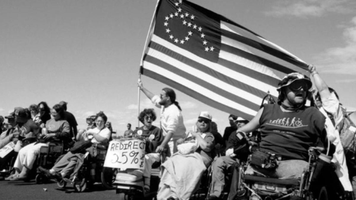 Disability activists hold American flag in which the stars form the shape of a wheelchair user