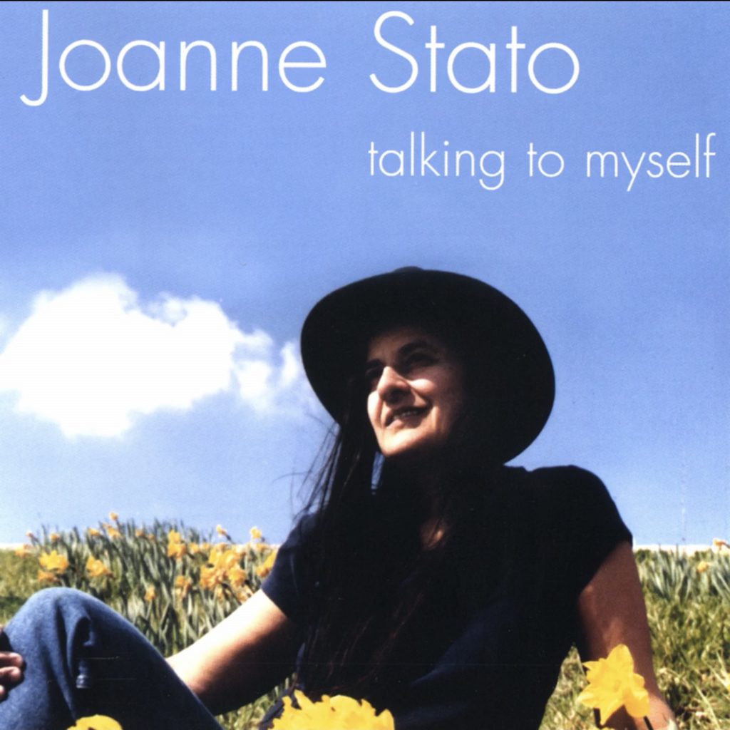 Album cover shows Joanne sitting in a field of yellow flowers with a big blue sky behind her. The words “Joanne Stato, Talking to Myself” appear in white letters against the sky.