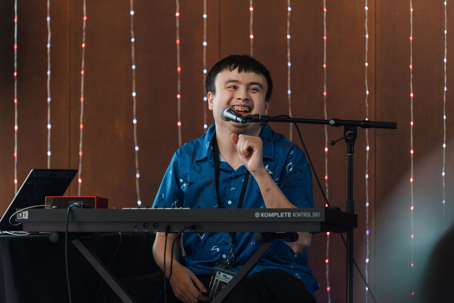 Devin Gutierrez smiles big on stage in front of the mic and his keyboard