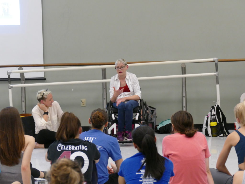 Tanya is sitting in her wheelchair on the right side of the photo with the rest of the Body Shift Collective dancers and teachers at the Texas Dance Improvisational Festival. Tanya in front of students telling the story of how she ended up in the dance world. Silva is sitting on the floor laughing.