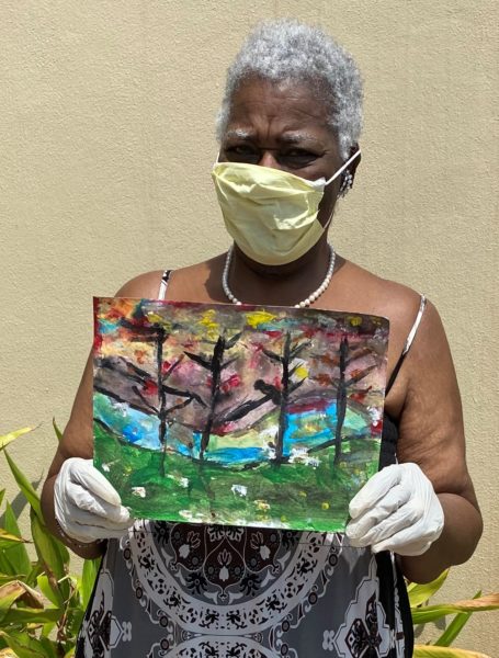 A woman wearing a mask and protective gloves holds a painting.