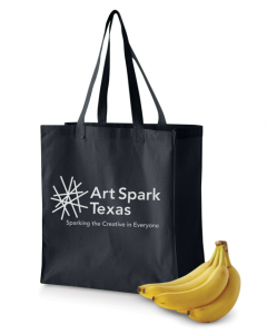 Black tote bag with a white Art Spark Texas logo placed next to ripe bananas in front of a white background 