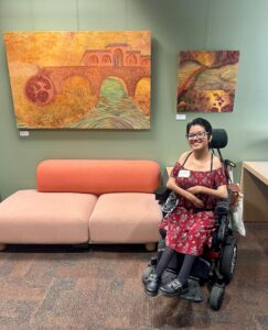 Artist Rachel Salcido in front of their artwork at the Disability Cultural Center for the solo art exhibit Cuerpos Fronterizos