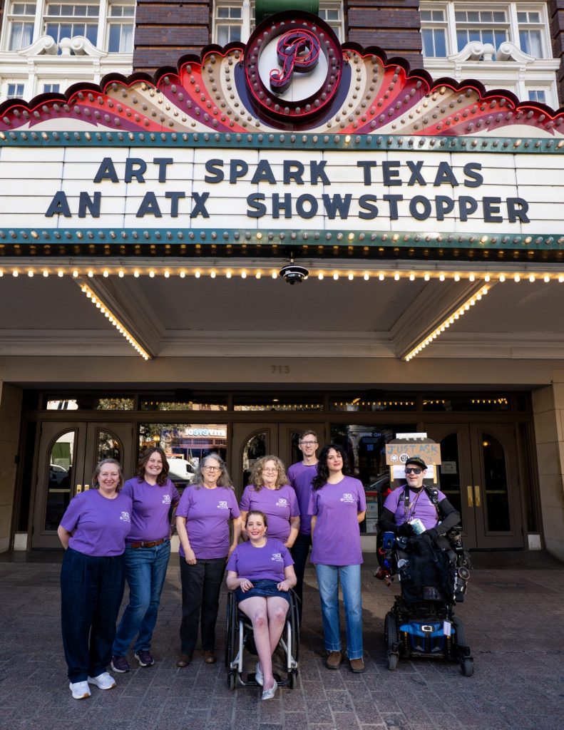 Art Spark Texas and friends wear their purple 30th anniversary t-shirts and pose in front of the historic Paramount marquee highlighting the organization