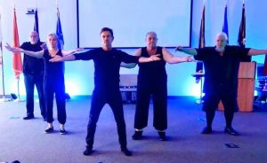 five dancers pose standing with their arms stretched out to their sides