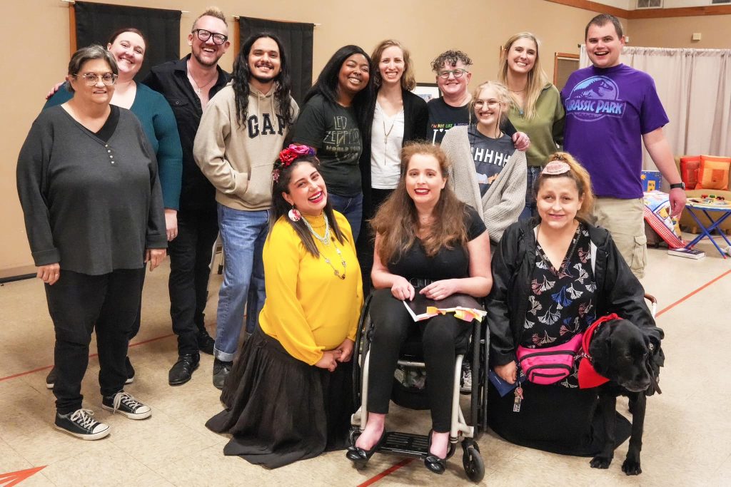 Yadira kneels bottom right of cast and crew smiling into camera with Deja, wearing a red bandanna, by her side.