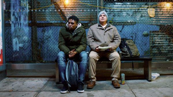 Photo of two men on a bus stop bench.