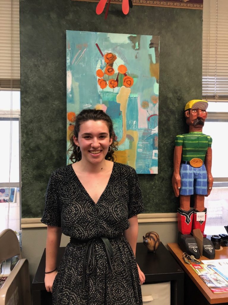 Grace standing in front of painting at the Art Spark office