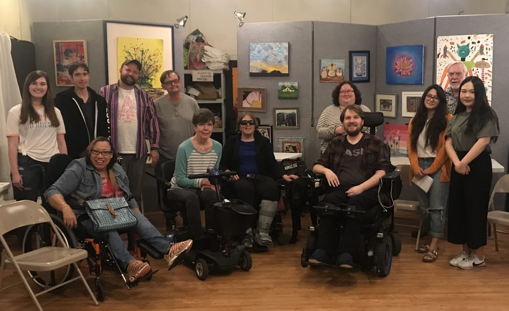 diverse group of adults with and without wheelchairs pose before panels with visual art
