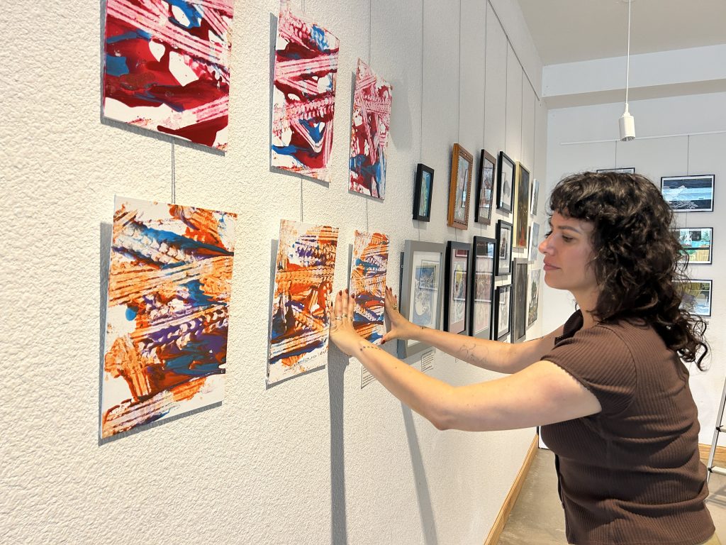 Kim Flor installing All for Art, Jonah Dillon's paintings at Imagine Art with Art Spark Texas community exhibition centering homeless and disabled artists