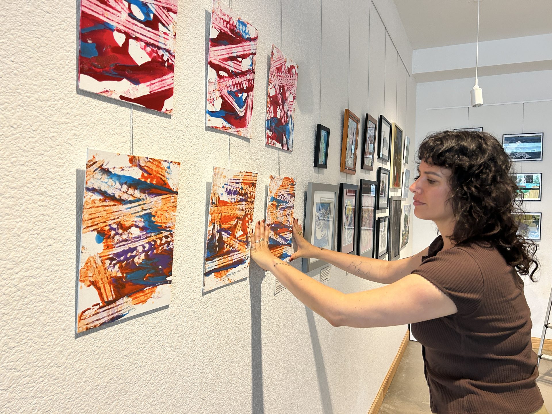 Kim Flor installing All for Art, Jonah Dillon's paintings at Imagine Art with Art Spark Texas community exhibition centering homeless and disabled artists