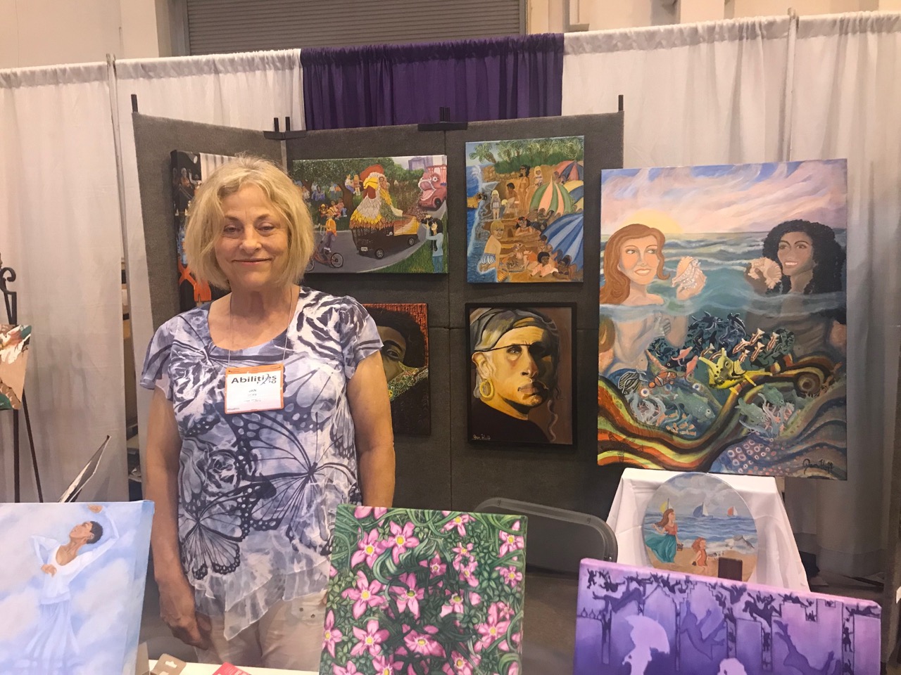 artist poses in front of her booth of artwork at abilities Expo