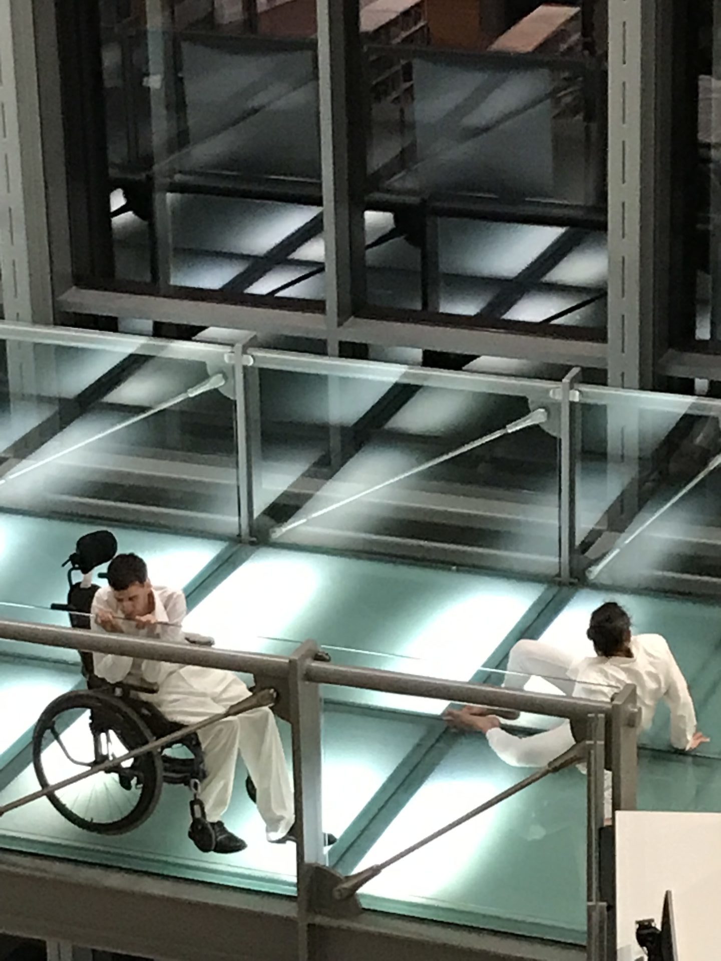 two dancers, one in a wheelchair, pose on a glass walkway