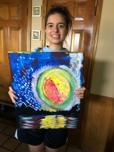 A person poses smiling with a painting they created.
