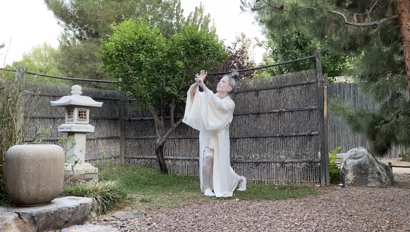 Woman dressed in white gown with her hair in a bun strikes a pose in a garden
