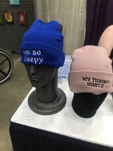 two beanie style hats with different text on the front. One reads, "I'm so sleepy." and the other reads, "My tummy hurts."