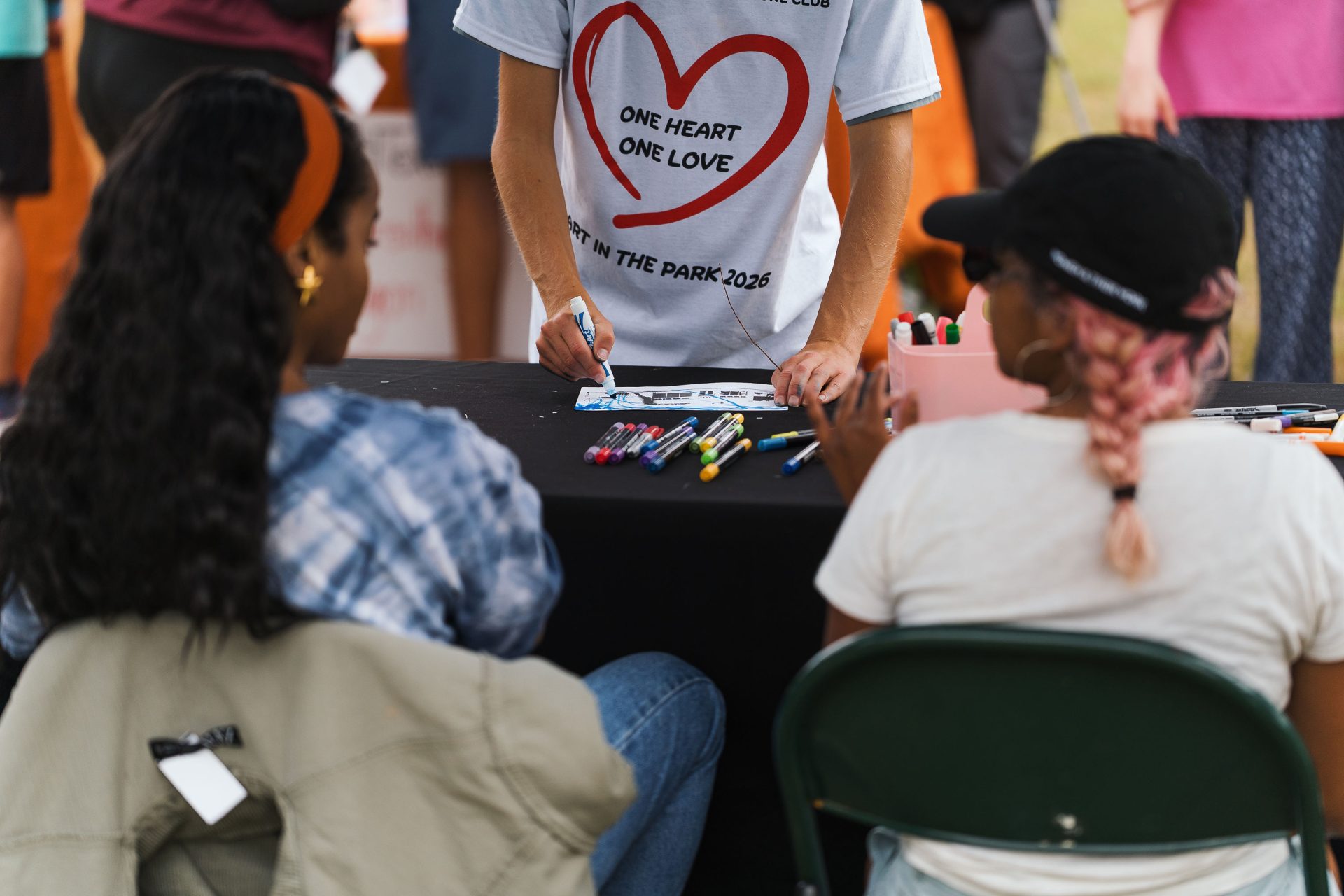 McBeth WINGS dancer approaches an art activity table at Art Spark Texas' Art in the Park wearing their 2026 Art in the Park t-shirts