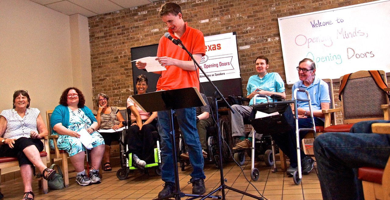 man gives speech with other speakers smiling in background