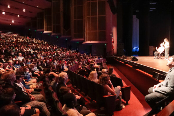 Dwayne and Sea on stage in front of a large, filled auditorium.