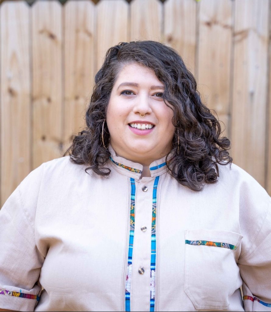 A person smiling while standing in front of a wooden fence.