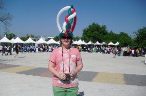 Person wearing a tall hat made from balloons stands smiling, posing for a picture.