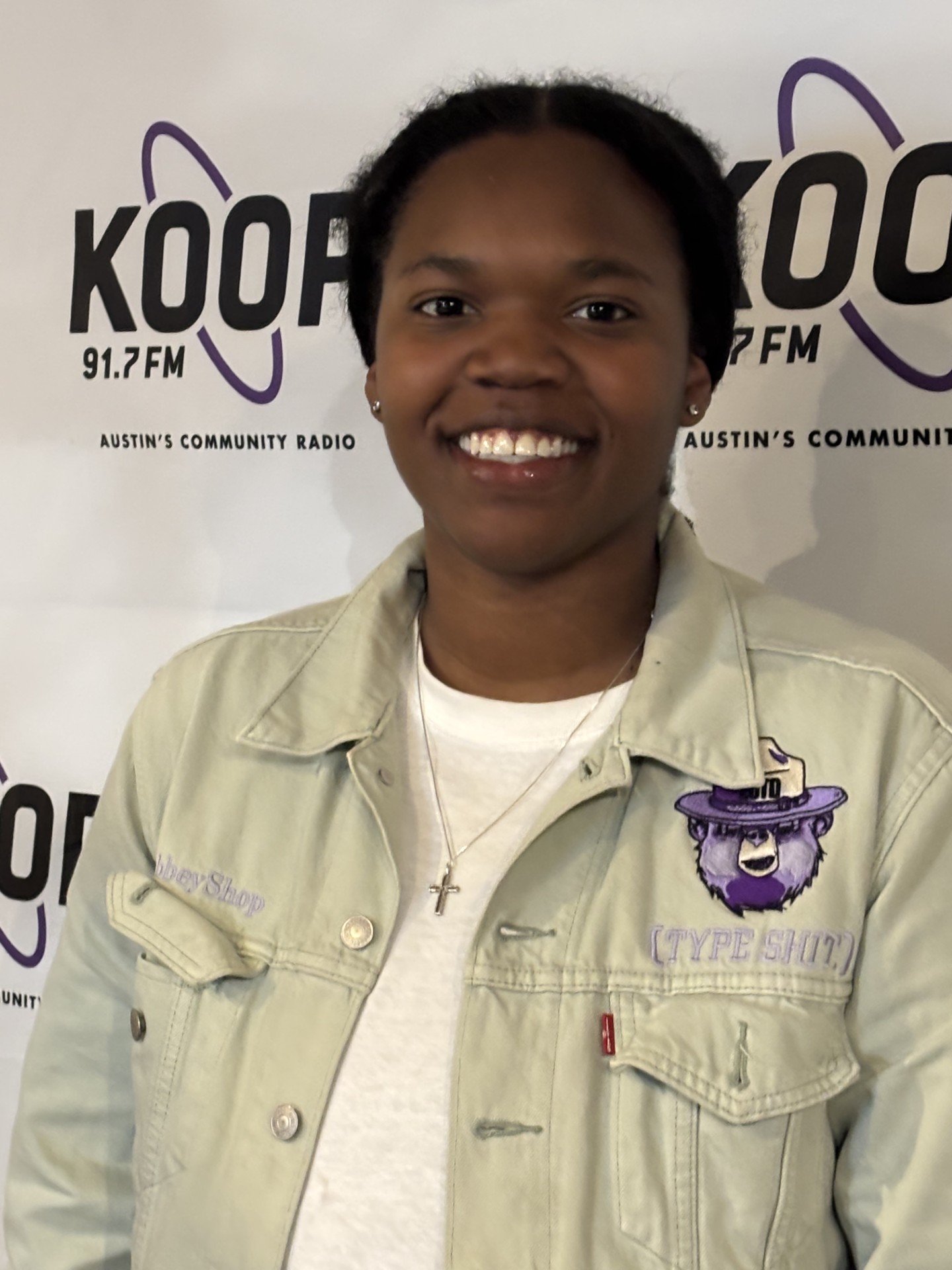 KOOP Radio's Art Spark Texas Radio Hour 2026 Intern Jaela Mitchell stands in front of the KOOP studio backdrop
