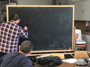 photo of Veteran writing instructor Clayton Bradshaw writing on the blackboard in a writing class