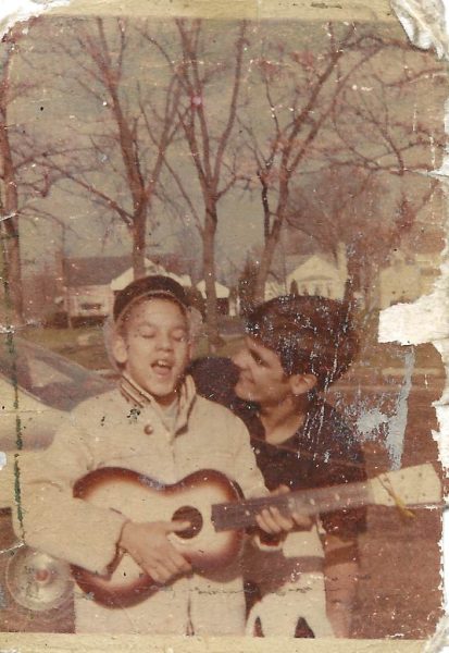 An aged color photo shows Jeff as a child strumming a miniature guitar and singing with an older relative behind him.