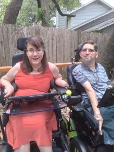 Dave and Kate, seated side by side in power wheelchairs, smile for the camera.