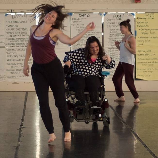 Amy dances in her wheelchair with two non-disabled women. All are smiling.