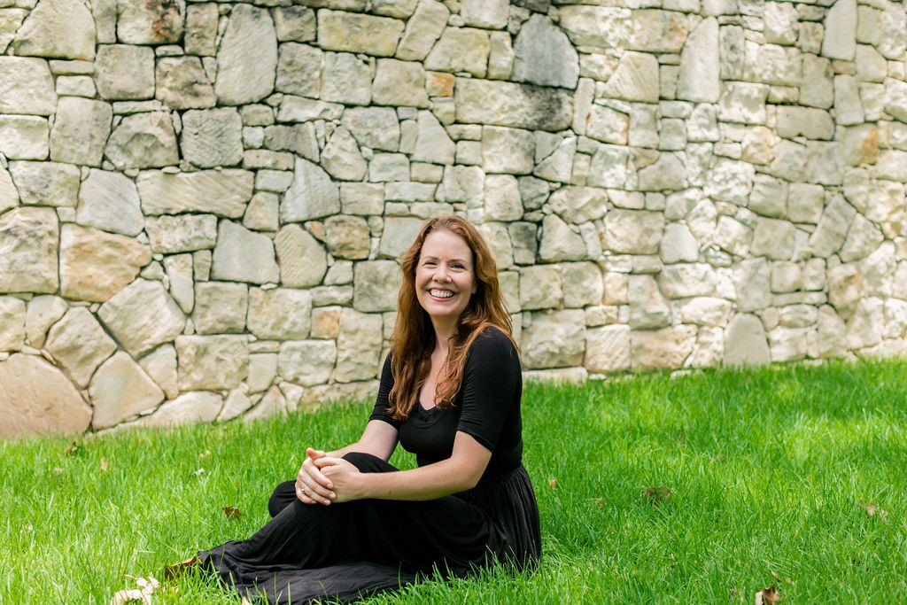 Woman sitting on a green grass in front of a brick wall.