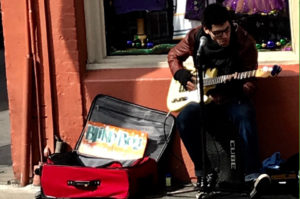 musician playing guitar sitting on the street in front of store window