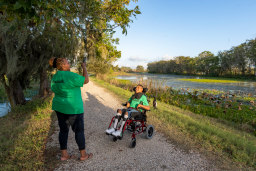 An adult taking a photo of a child in a wheelchair in a park