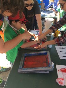 A child participates in a screen printing activity while 3 adults watch.