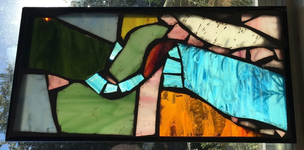 A framed abstract stained glass piece in a window