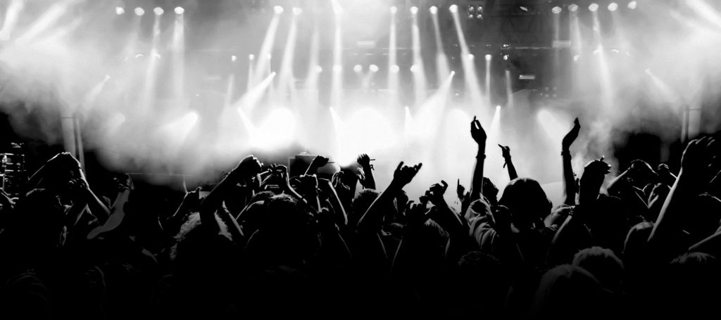 Black and white photo of crowd dancing and holding arms up in the air during a concert